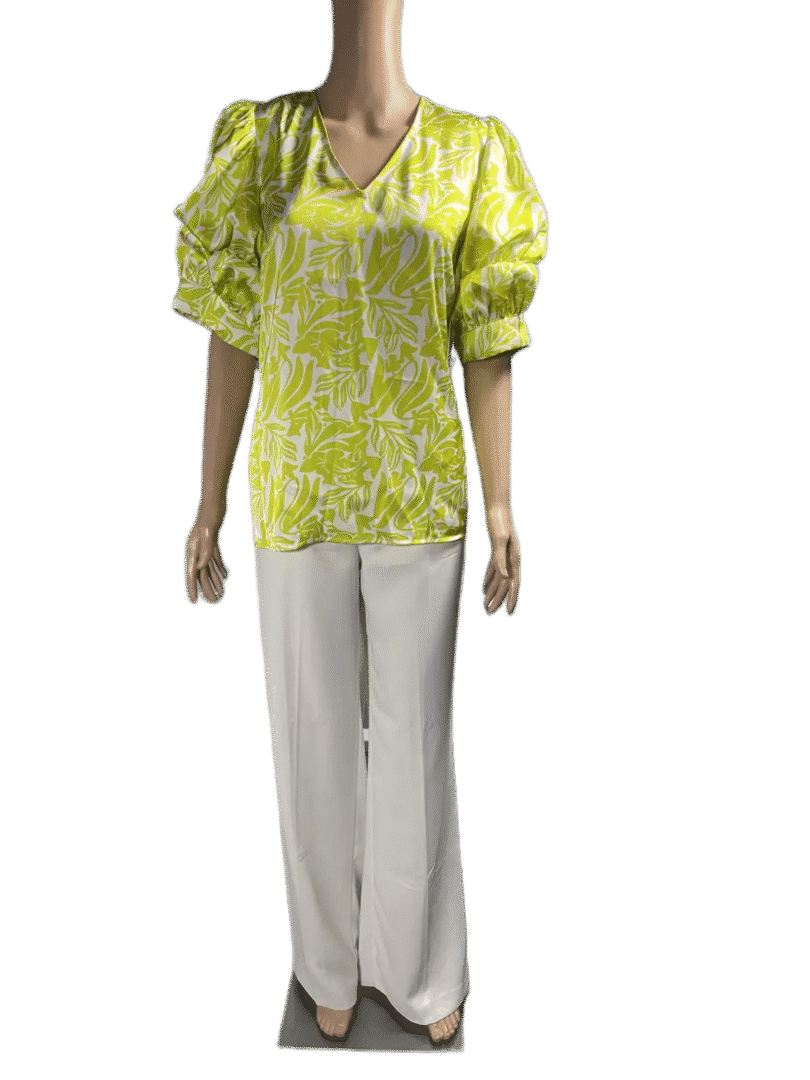 Woman wearing a green patterned blouse and white pants.